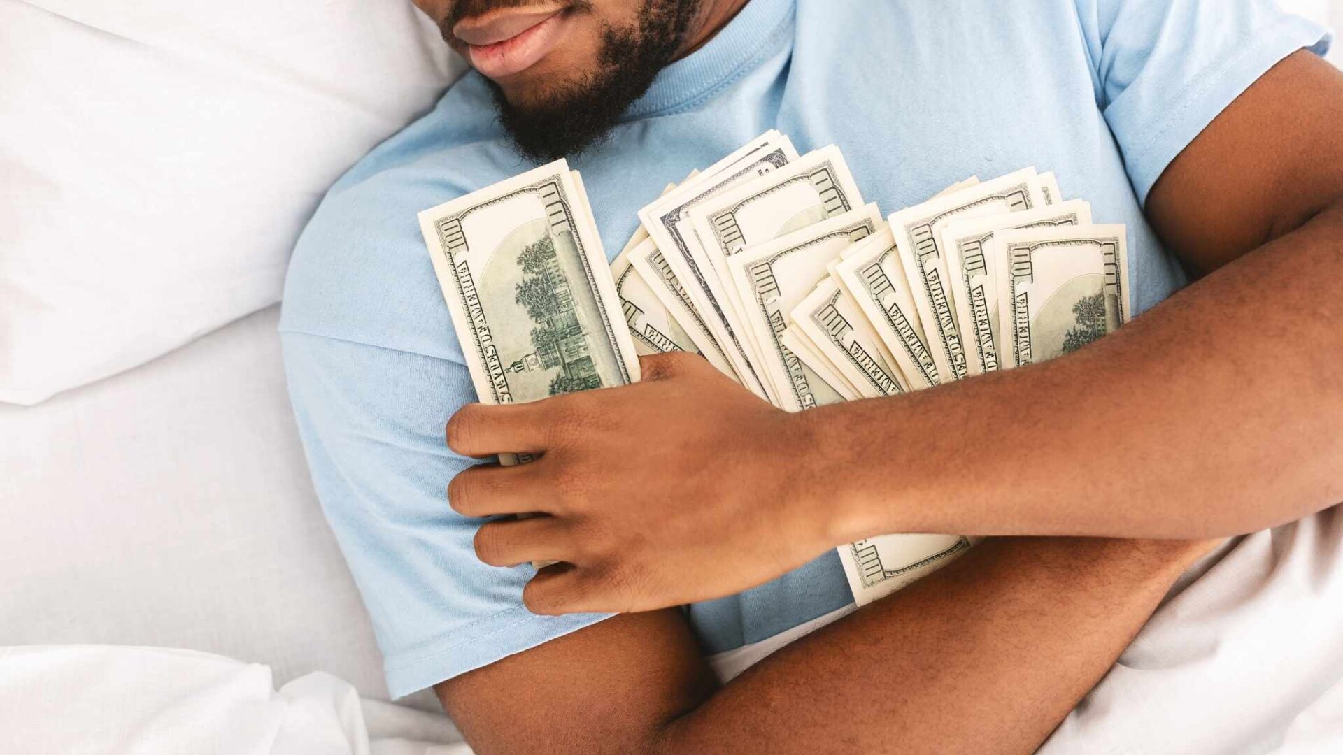 Hombre abrazando varios billetes de dinero en la cama simbolizando abundancia, riqueza y sueños relacionados con dinero