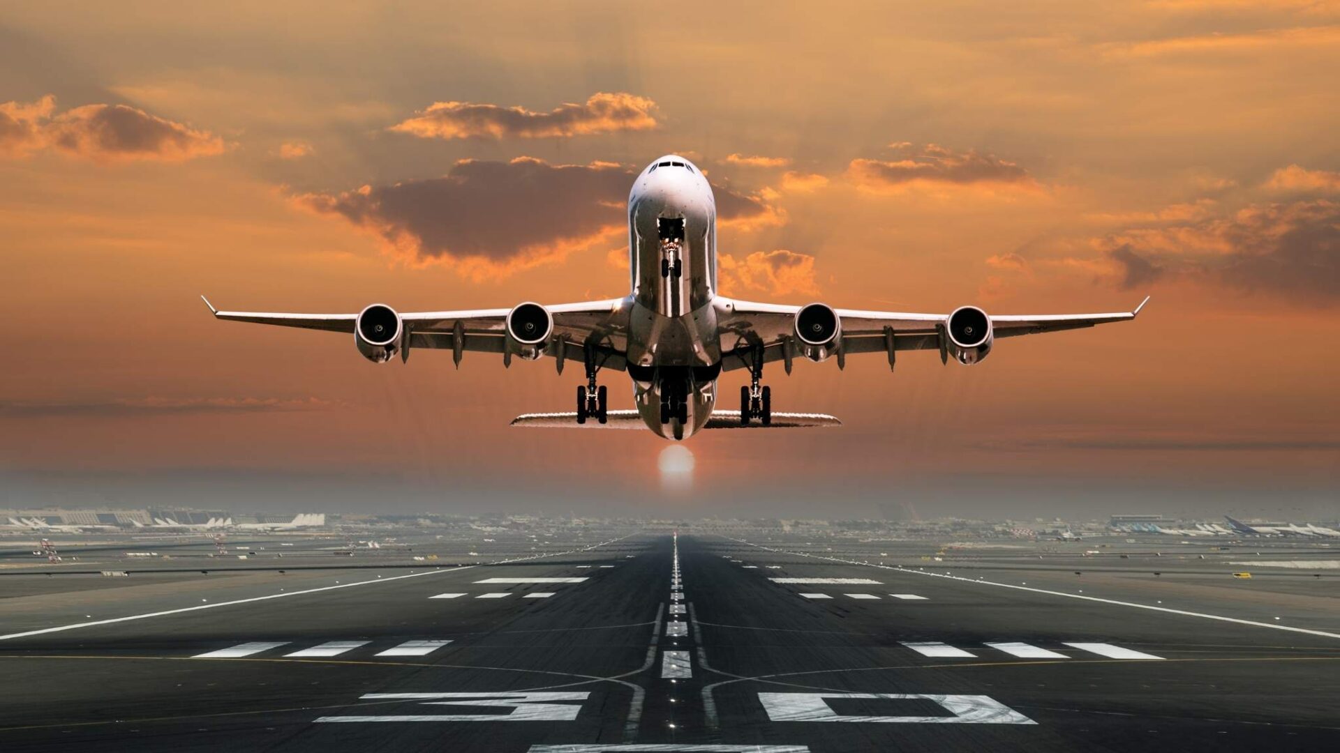 Avión despegando en una pista al atardecer con cielo naranja y vista frontal impactante