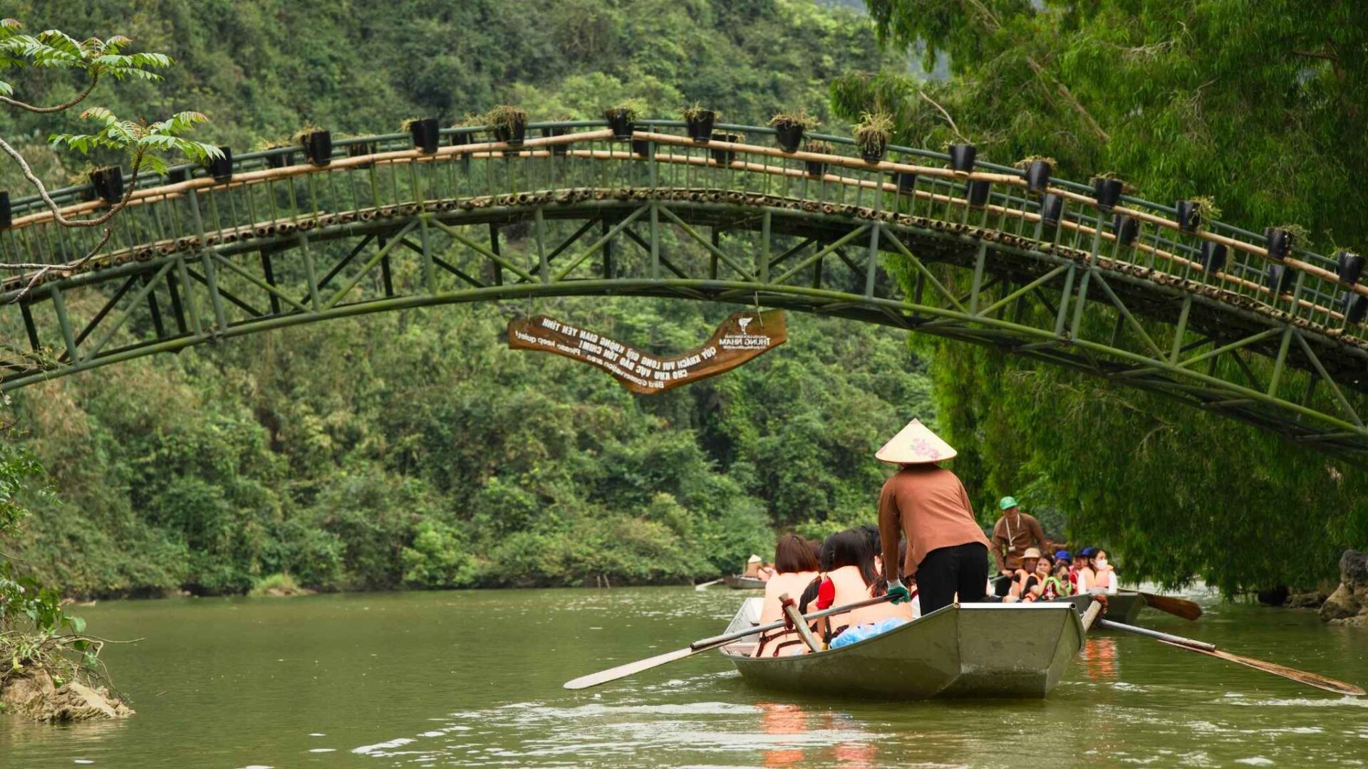 Paseo en barca bajo un puente de bambú rodeado de naturaleza exuberante y río tranquilo
