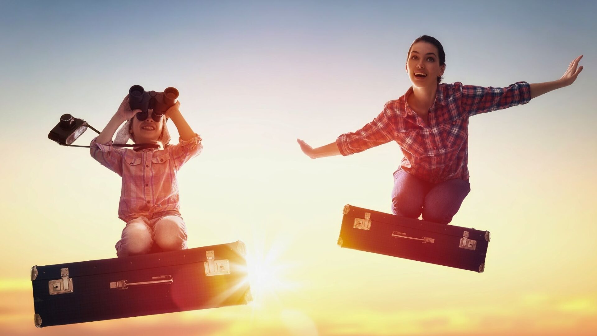 Madre e hijo sobre maletas simulando volar con binoculares en escena de viaje y aventura
