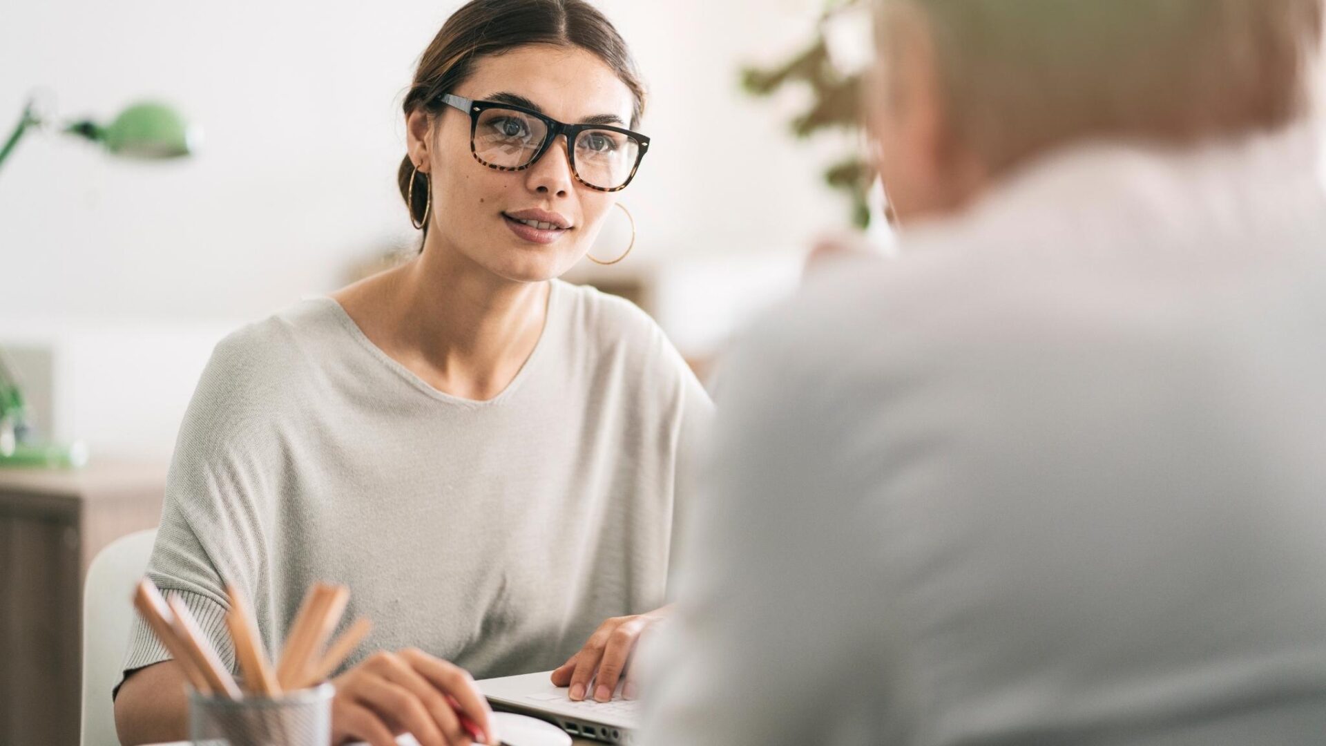 Mujer con gafas en reunión profesional hablando con otra persona en oficina moderna y ambiente corporativo