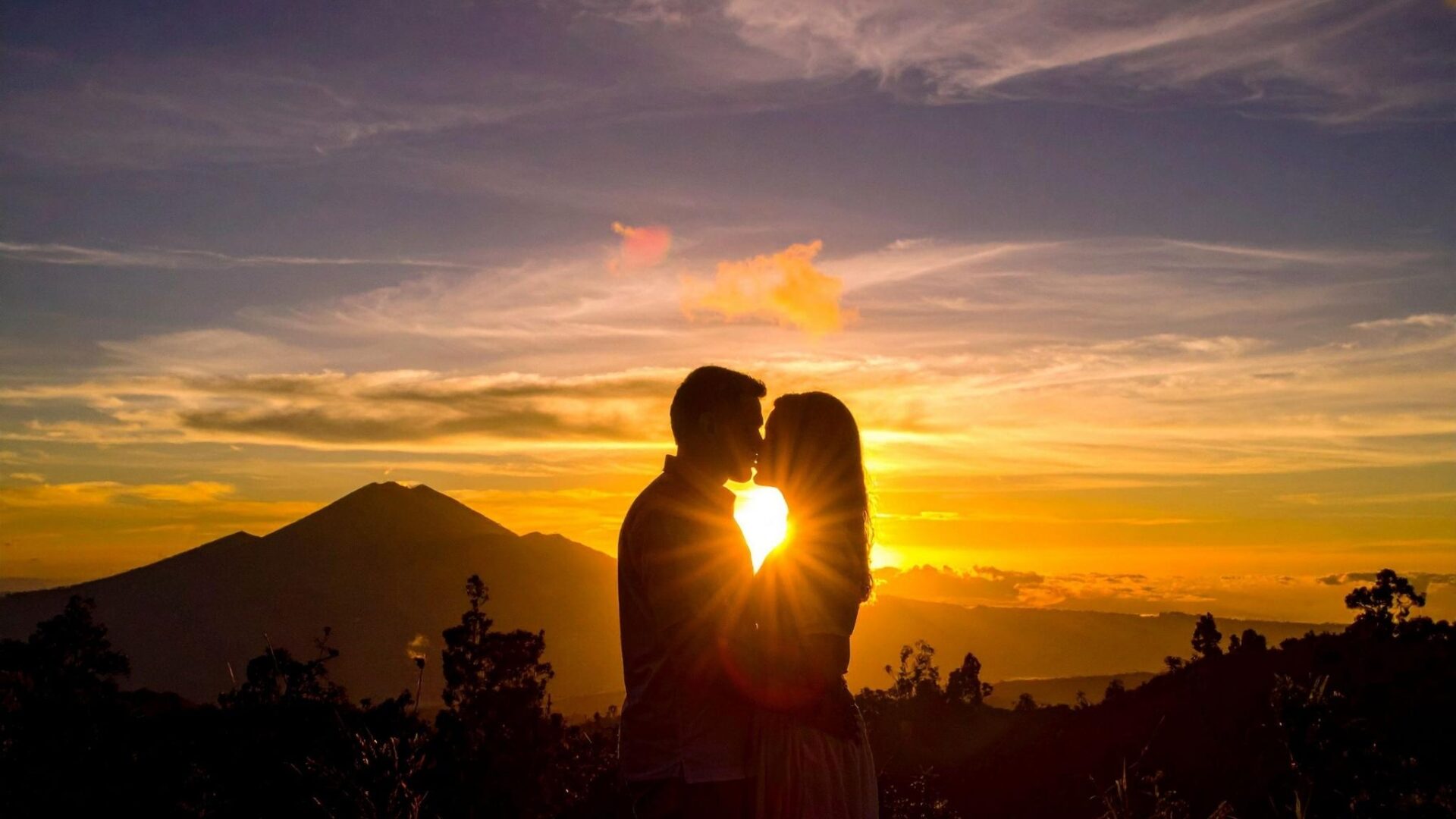 Pareja besándose al atardecer frente a una montaña con el sol de fondo, imagen relacionada con soñar con besos y su significado
