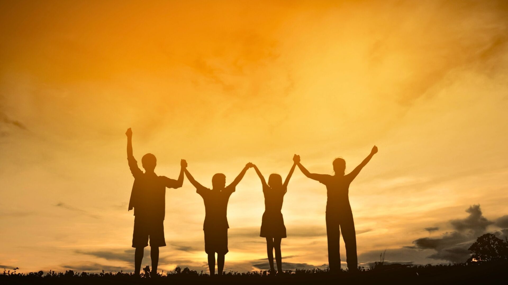 Silueta de una familia tomada de las manos al atardecer con un cielo dorado, representando unión, reconciliación, esperanza y felicidad compartida.