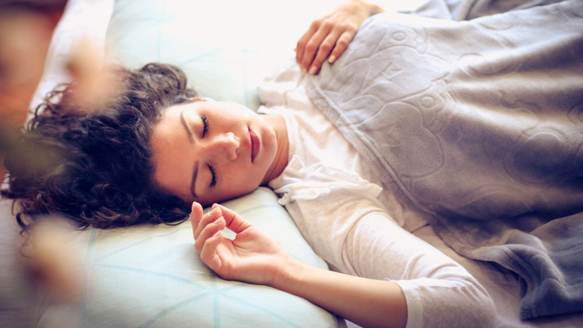 Mujer joven durmiendo tranquilamente en una cama con una manta gris, representando el descanso, los sueños y la interpretación de experiencias oníricas durante el sueño.